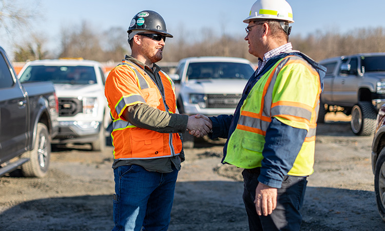 Two men in hard hats and construction vests shaking hands
